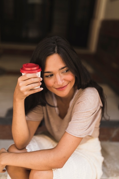 テイクアウトのコーヒーカップを持っている笑顔の少女