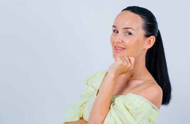 Smiling girl i sposing to camera by holding hand on cheek on white background