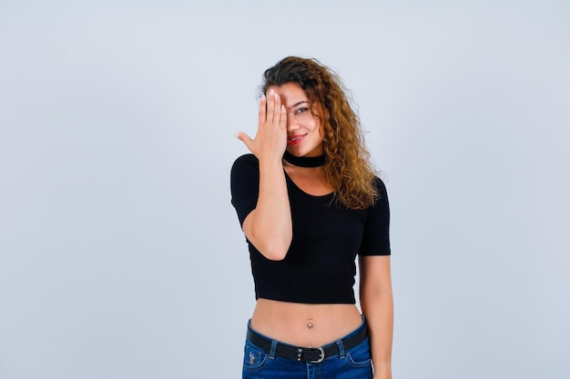 Smiling girl is covering her left side of face with hand on white background