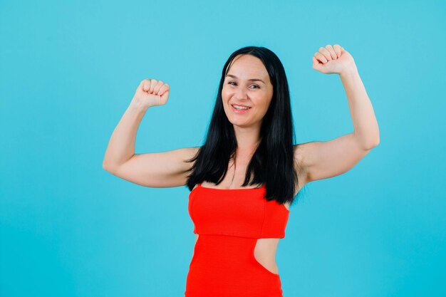 Smiling girl is dancing by raising up her fists on blue background