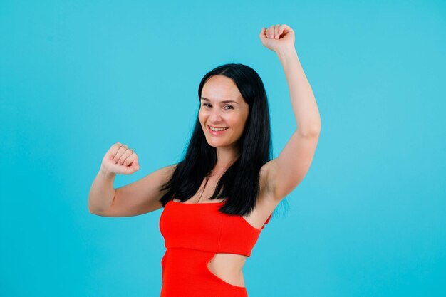 Smiling girl is danving by raising up her hands on blue background