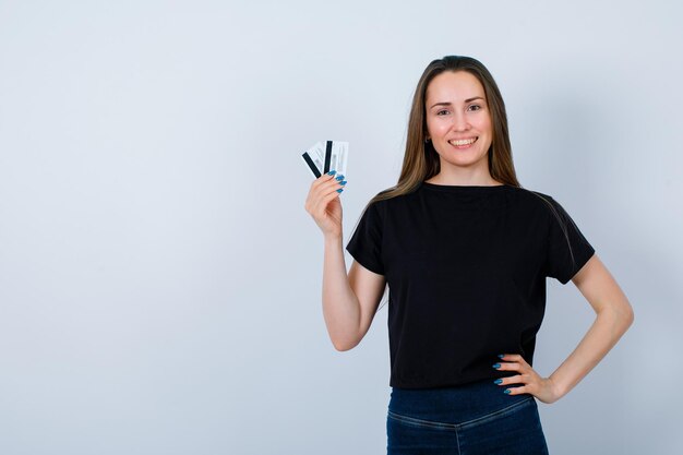 Smiling girl is holding credit cards and putting other hand on waist on white background
