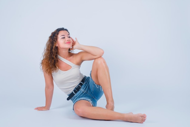 Foto gratuita la ragazza sorridente sta distogliendo lo sguardo tenendo la mano sulla guancia su sfondo bianco