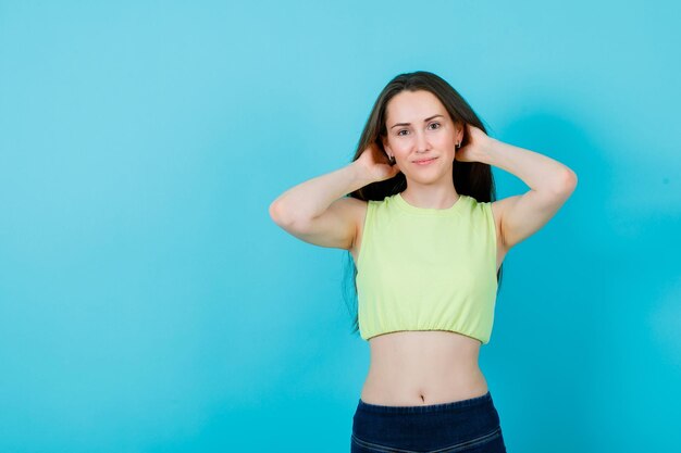 Smiling girl is looking away by holding hands behind head on blue background