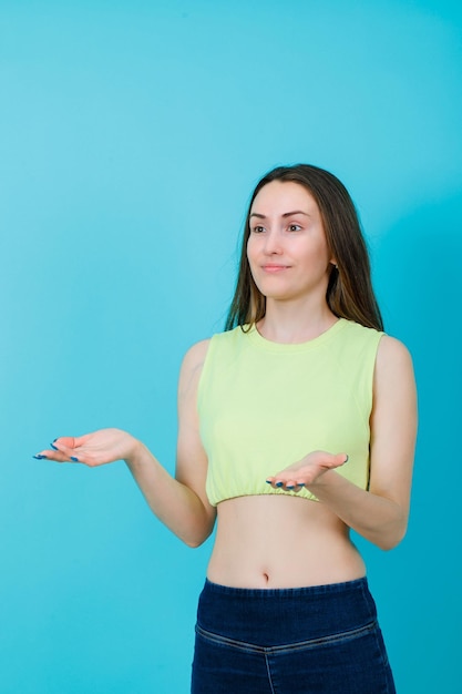 Smiling girl is looking away by opening wide her handfuls on blue background