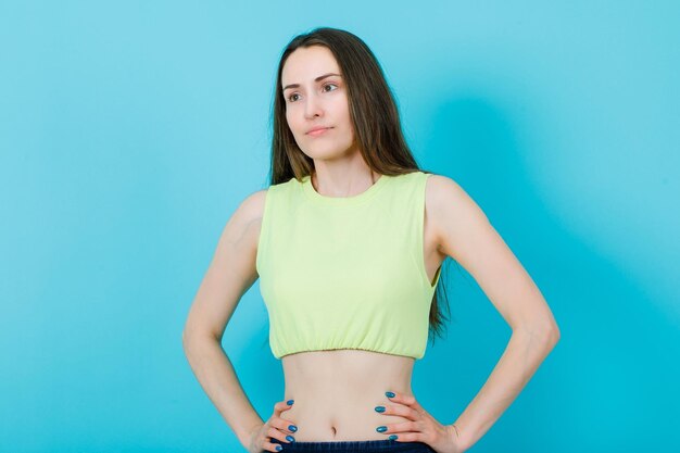 Smiling girl is looking away by putting hands on waist on blue background