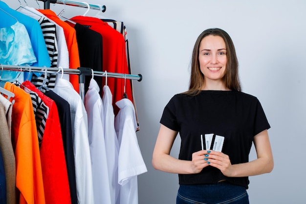 La ragazza sorridente sta esaminando la macchina fotografica tenendo le carte di credito sullo sfondo dei vestiti