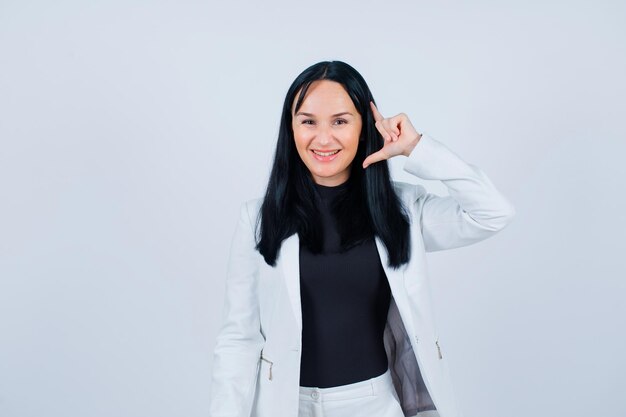 Smiling girl is looking at camera by holding fingers near ear on white background