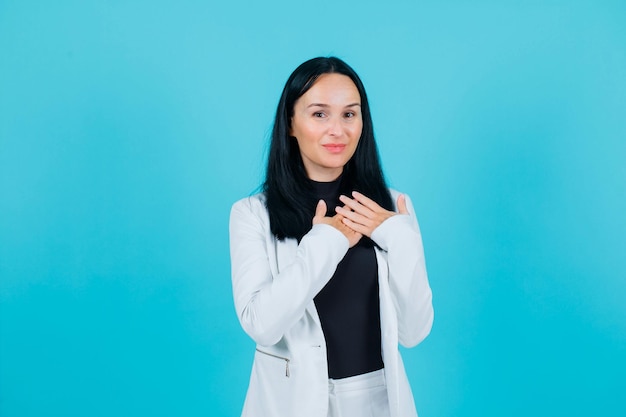 Smiling girl is looking at camera by holding hands on shoulder on blue background