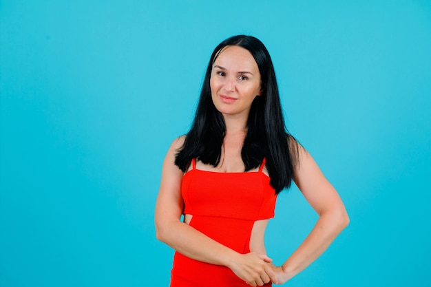 Smiling girl is looking at camera by holding hands together on waist on blue background