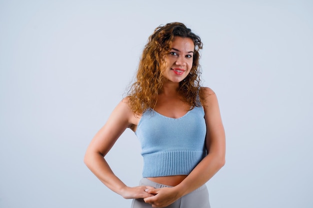 Smiling girl is looking at camera by holding hands together on waist on white background