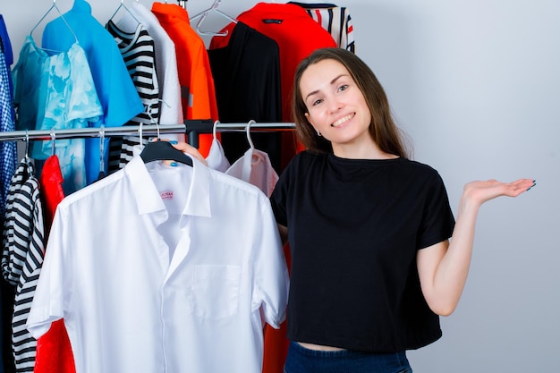Free photo smiling girl is looking at camera by holding shirt on clothes background