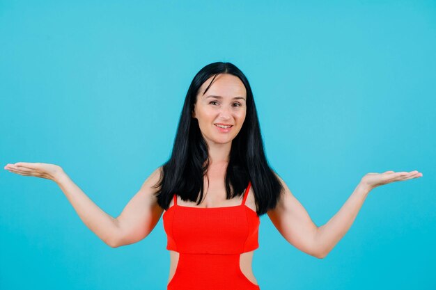 Smiling girl is looking at camera by opening wide her arms on blue background