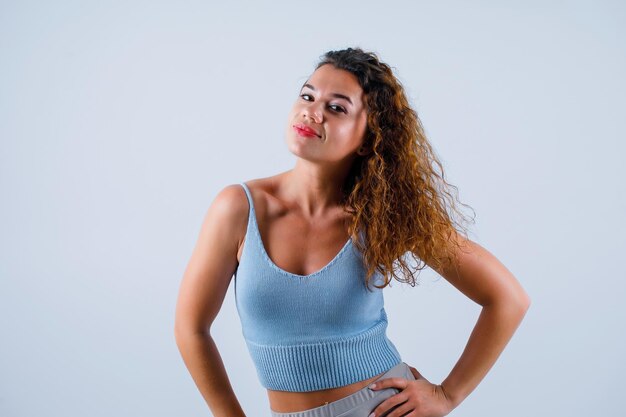 Smiling girl is looking at camera by putting hands on waist on white background