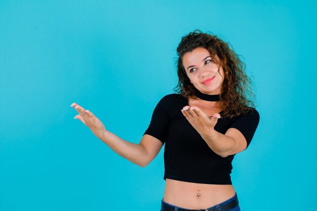 Smiling girl is looking left by extending hands on blue background