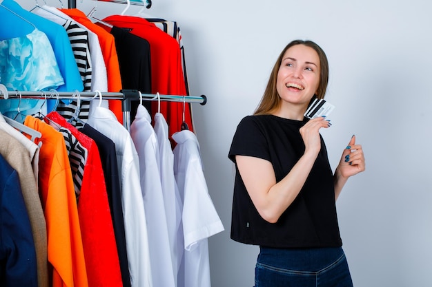 Smiling girl is looking up by holding credit card on clothes background