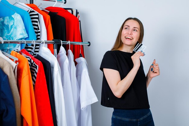 Smiling girl is looking up by holding credit card on clothes background