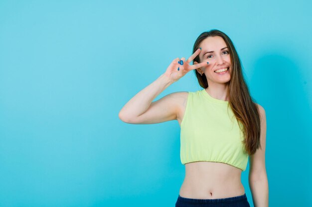 Smiling girl is looking up by showing two gesture on blue background