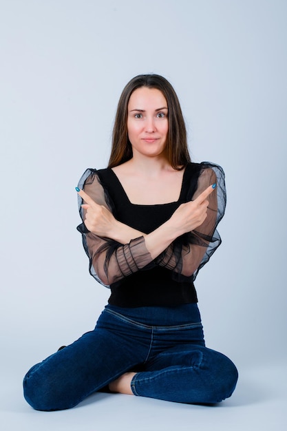 Smiling girl is pointing around by crossing arms on white background