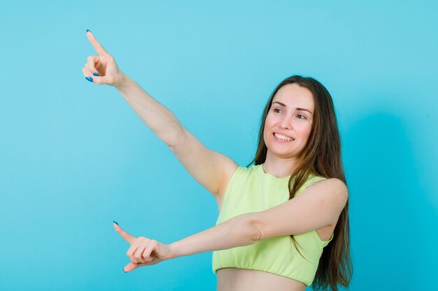 Smiling girl is pointing away with forefingers on blue background