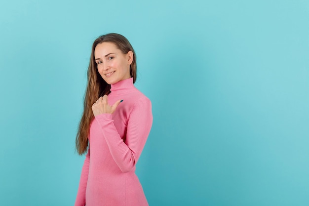 Smiling girl is pointing back with thumb on blue background