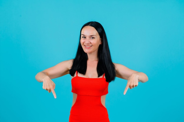 Smiling girl is pointing down with forefingers on blue background