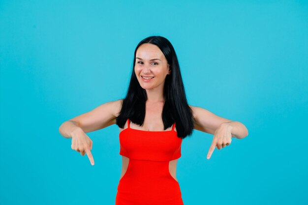 Smiling girl is pointing down with forefingers on blue background