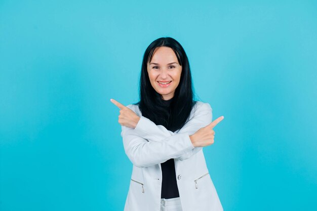 Smiling girl is pointing right and left with crossed arms on blue background