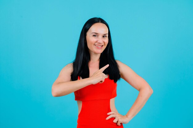 Smiling girl is pointing right with forefinger on blue background