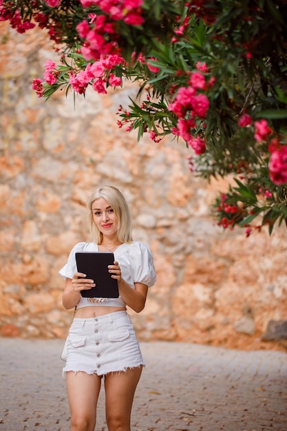 Smiling girl is posing to camera by holding planshet on stone background