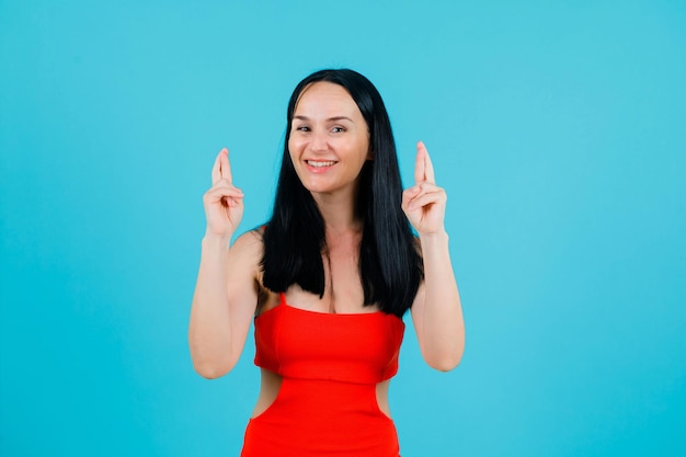 Smiling girl is raising up gher crossed fingers on blue background