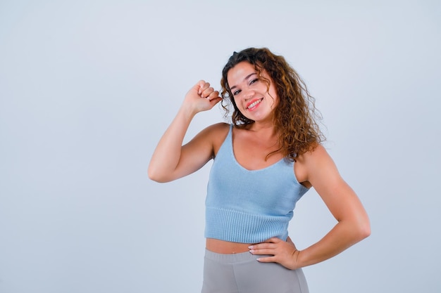 Smiling girl is raising up her fist and putting hand on waist on white background