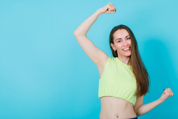 Smiling girl is raising up her fists on blue background