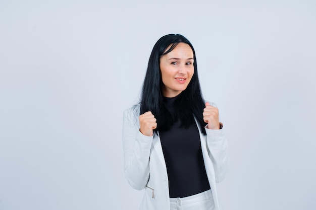 Smiling girl is raising up her fists on white background