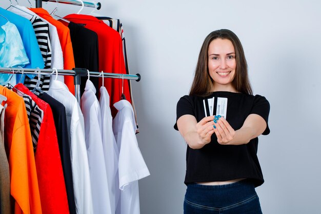 Улыбающаяся девушка показывает кредитные карты в камеру на фоне одежды