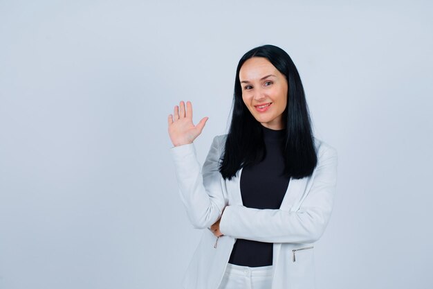 Smiling girl is showing hi getsure by raising up her hand on white background