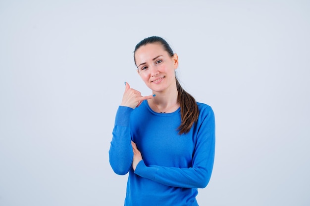 Smiling girl is showing mobile gesture by holding hand near ear on white background