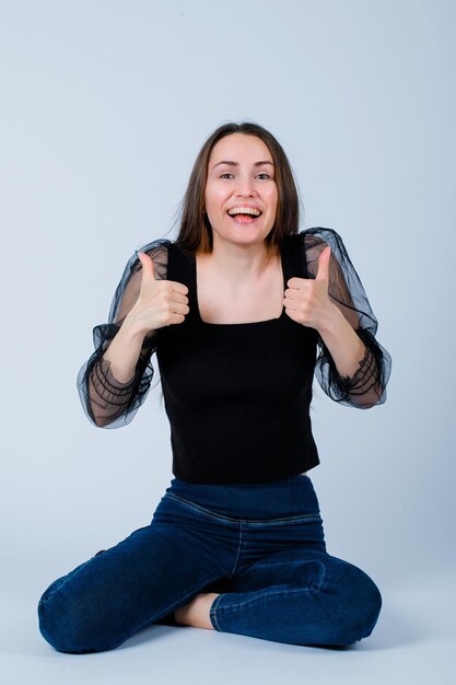 Smiling girl is showing perfect gestures by sitting on floor on white background