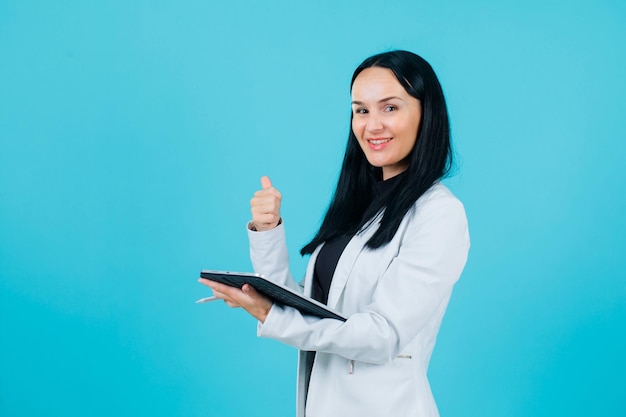 Smiling girl is showing perfect getsure by holding tablet on blue background