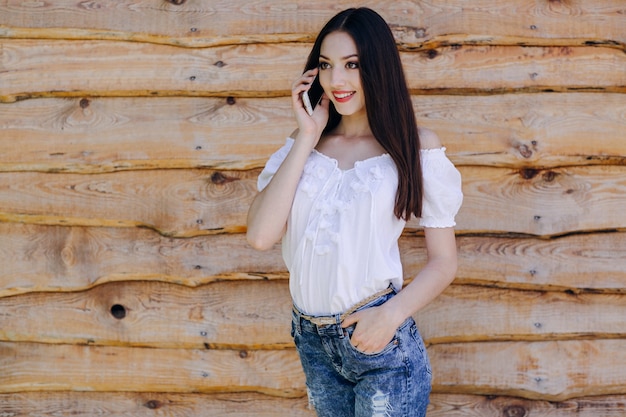 Smiling girl leaning on a wooden wall talking on the phone