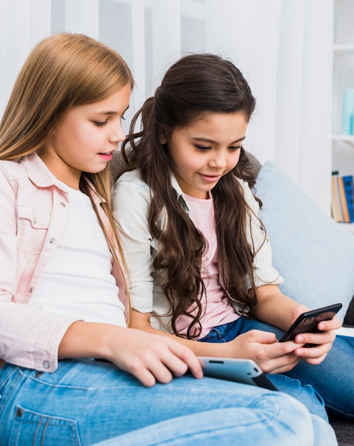 Free photo smiling girl looking at her friend using mobile phone