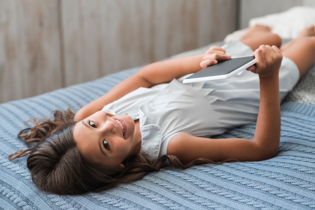 Smiling girl lying on bed holding digital tablet in hand