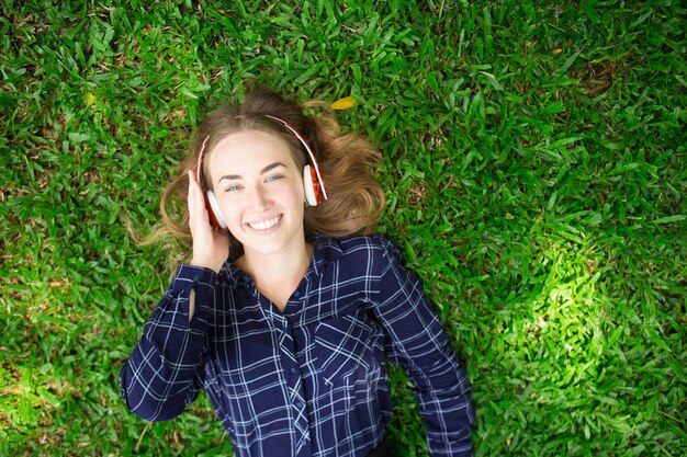 笑顔の女の子、草の上に横たわり、ヘッドフォンを着用