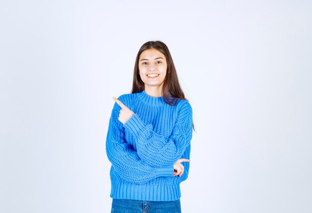 Smiling girl model pointing up and looking forward on gray white.