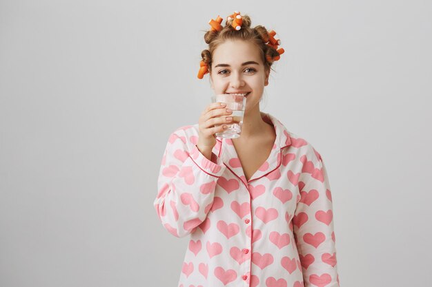 ヘアカーラーを使用してナイトウェア飲料水で笑顔の女の子