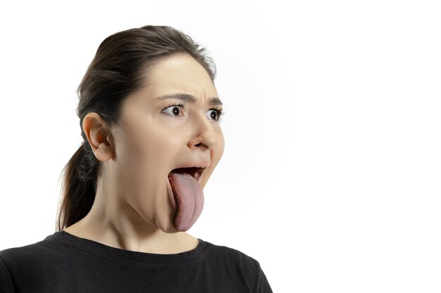 Smiling girl opening her mouth and showing the long big giant tongue isolated on white wall. Looks shocked, attracted, wondered and astonished. Copyspace for ad. Human emotions, marketing.