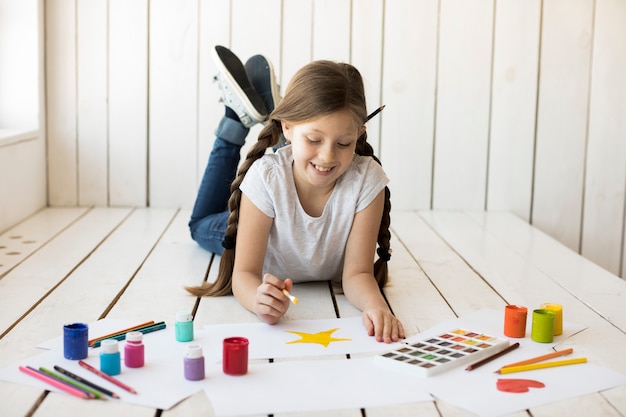 Free photo smiling girl painting the yellow star on white paper