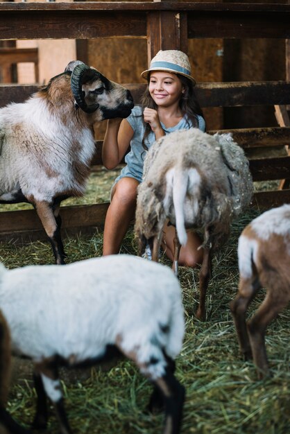 Smiling girl playing with sheep in the barn