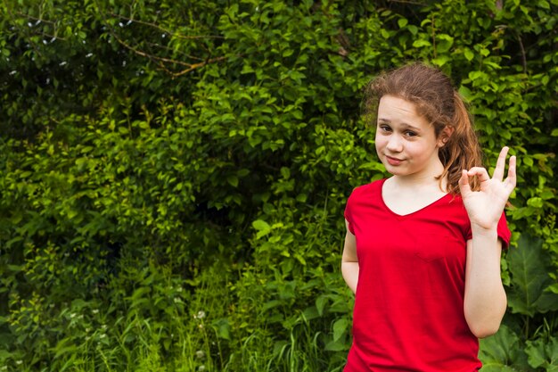 Smiling girl posing and showing ok gesture in park