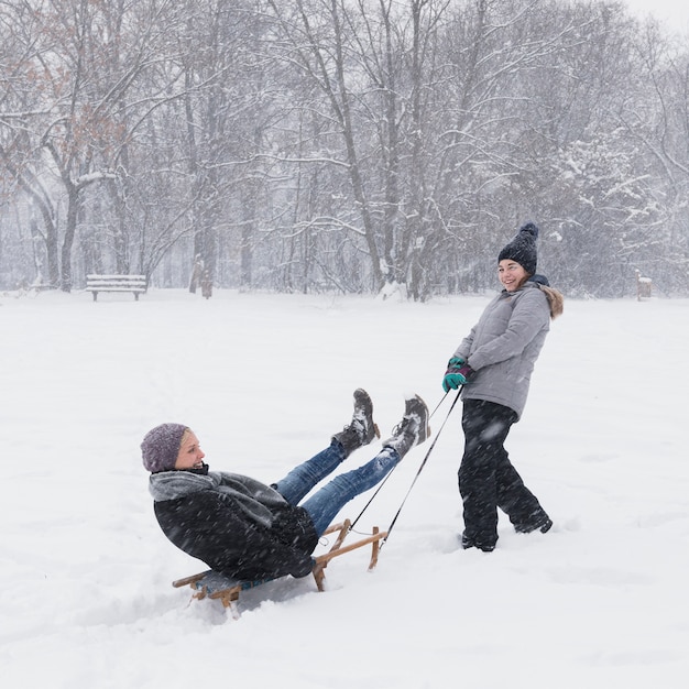 Free photo smiling girl pulling her mother on sledge at forest during snowing